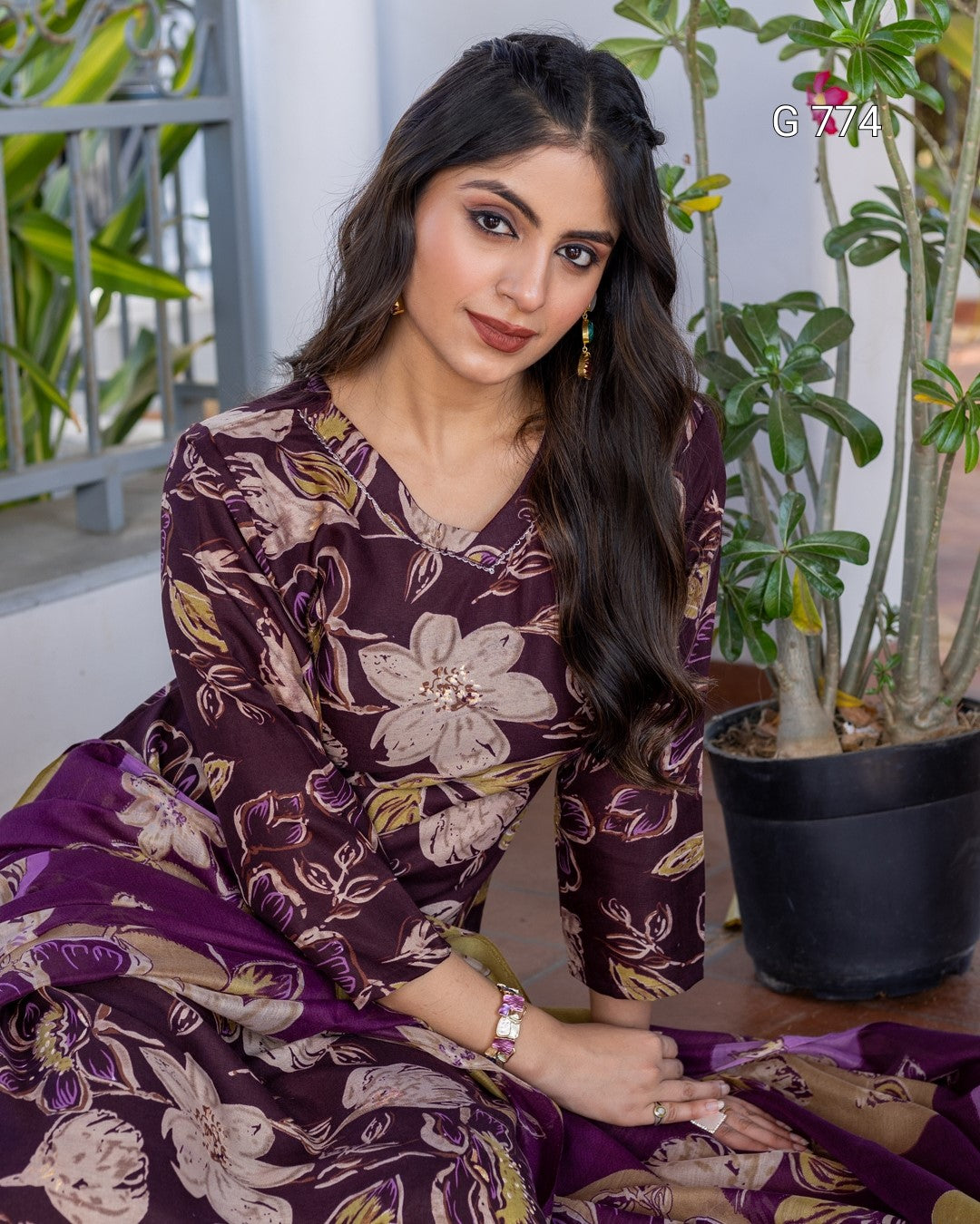 Woman wearing a purple floral dress sitting outdoors with plants in the background