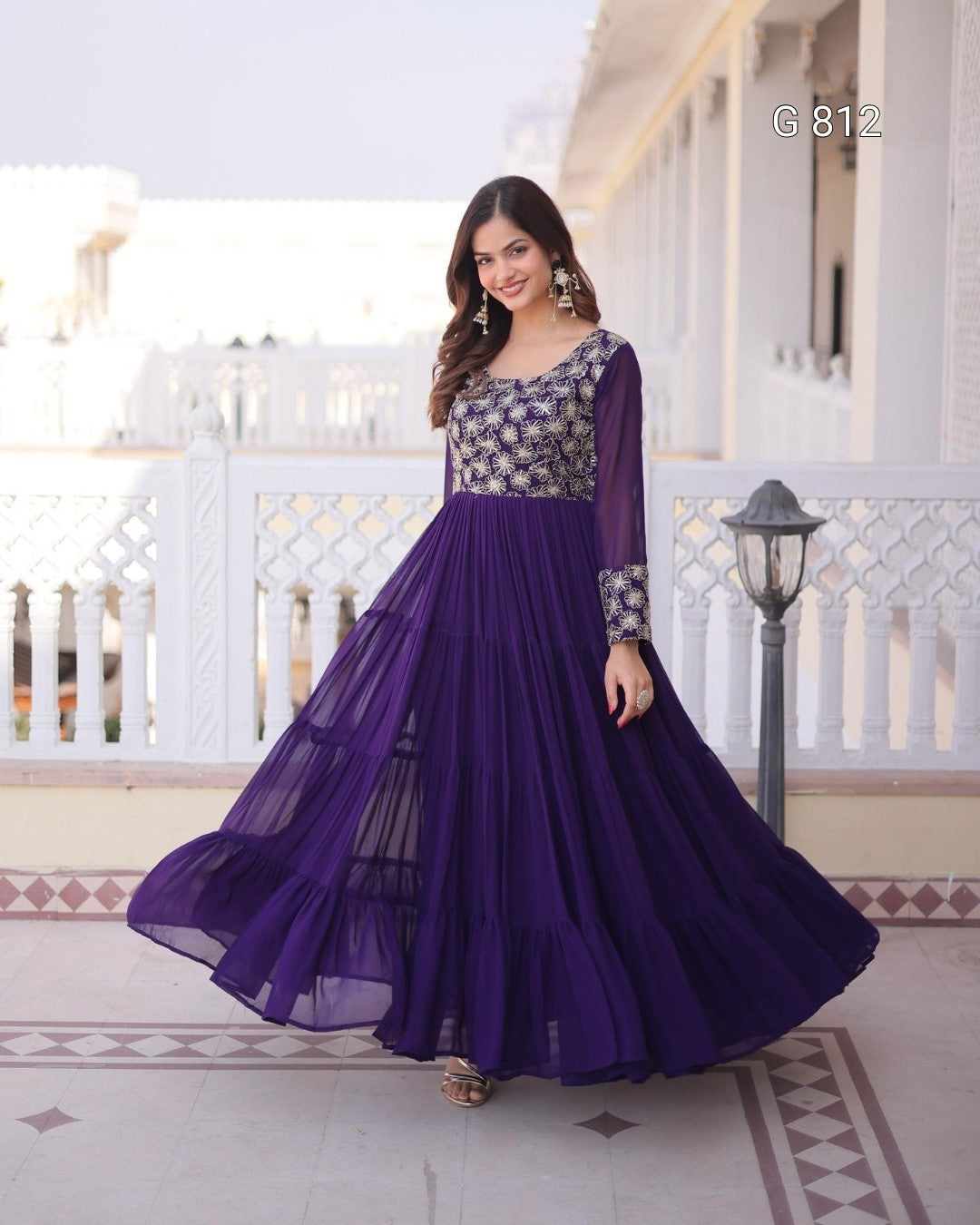 Woman in a purple and patterned top dress standing on a balcony.