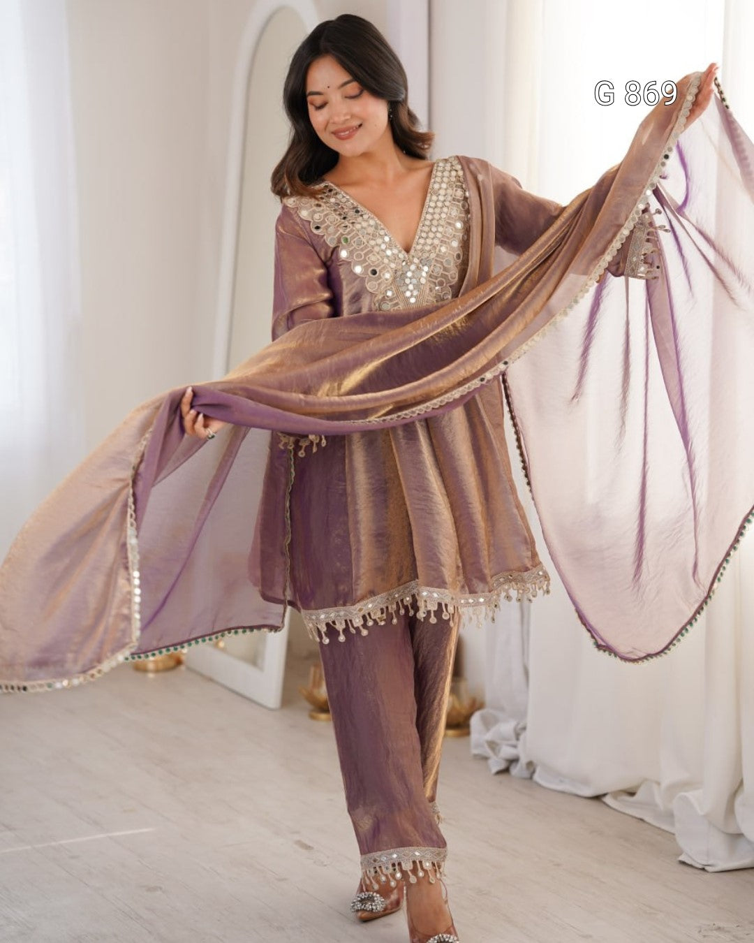 Woman in a traditional outfit with a sheer dupatta, standing indoors.