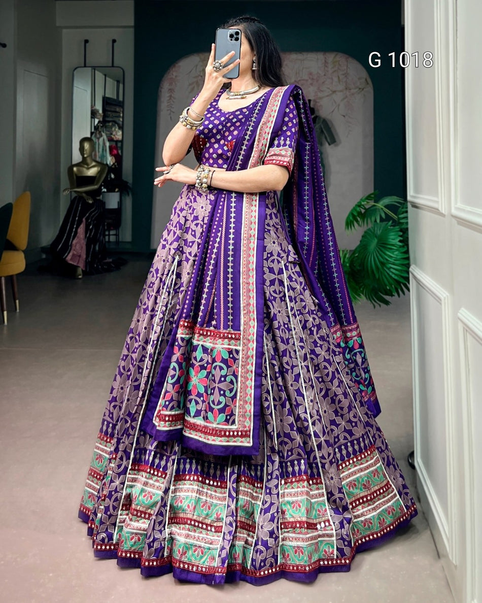 A woman takes a mirror selfie wearing a purple Indian ethnic lehenga choli set with intricate multicolor embroidery and patterns. The set features a purple flared skirt (lehenga), a matching embroidered blouse, and a coordinating dupatta.