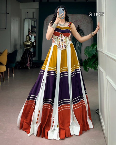 A woman takes a mirror selfie in a boutique wearing a sleeveless, floor-length A-line gown with a geometric color-blocked pattern in mustard yellow, white, purple, rust red, and black.
