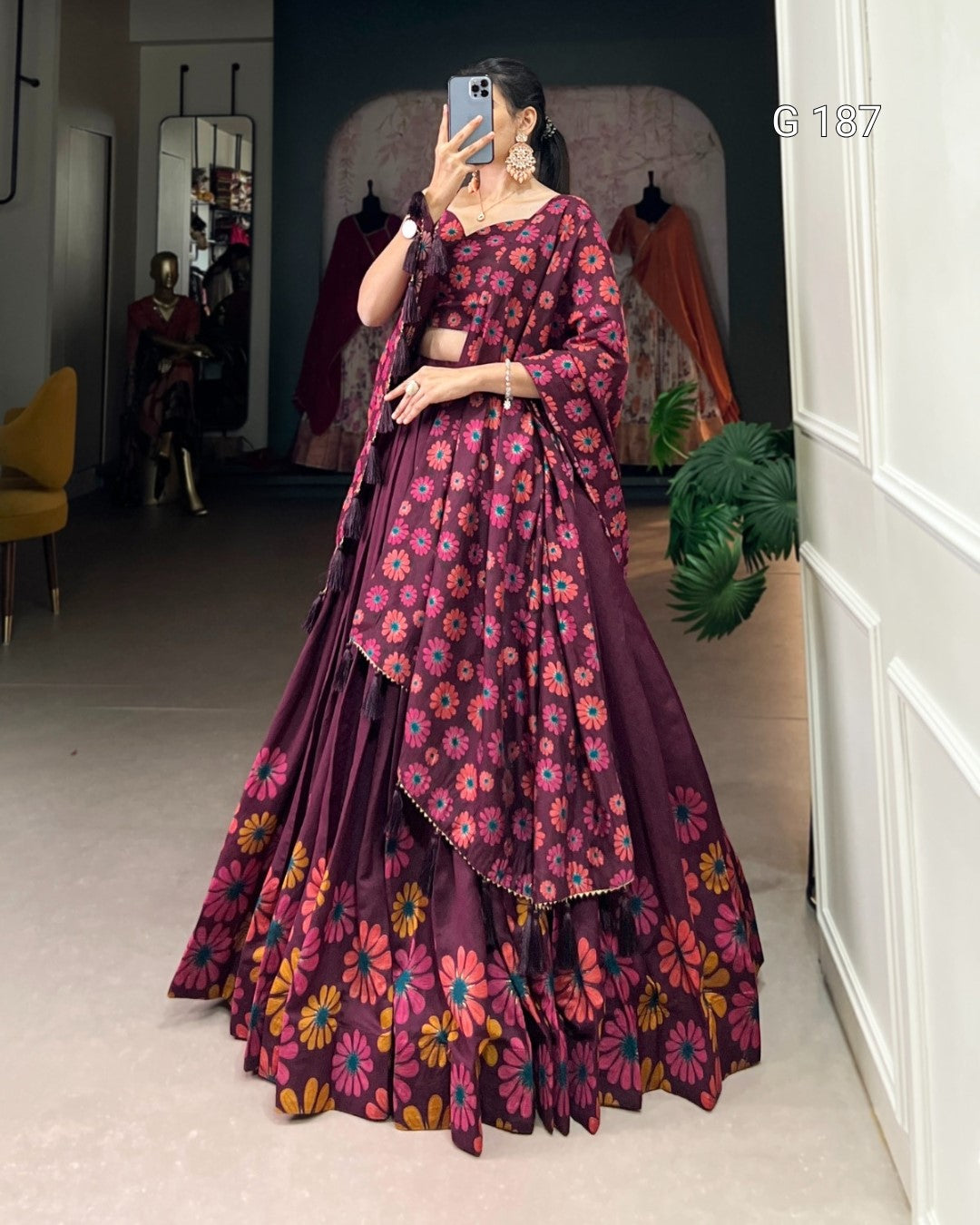 Woman wearing a purple floral saree in a room with a mirror and plant.