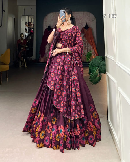 Woman wearing a purple floral saree in a room with a mirror and plant.