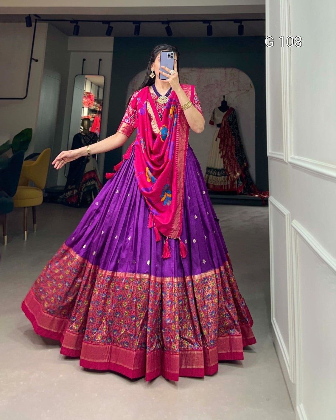 Person wearing a vibrant purple and pink traditional outfit with intricate designs indoors.