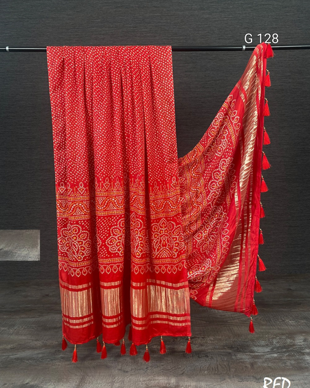 Red saree with gold patterns and tassels on a dark background