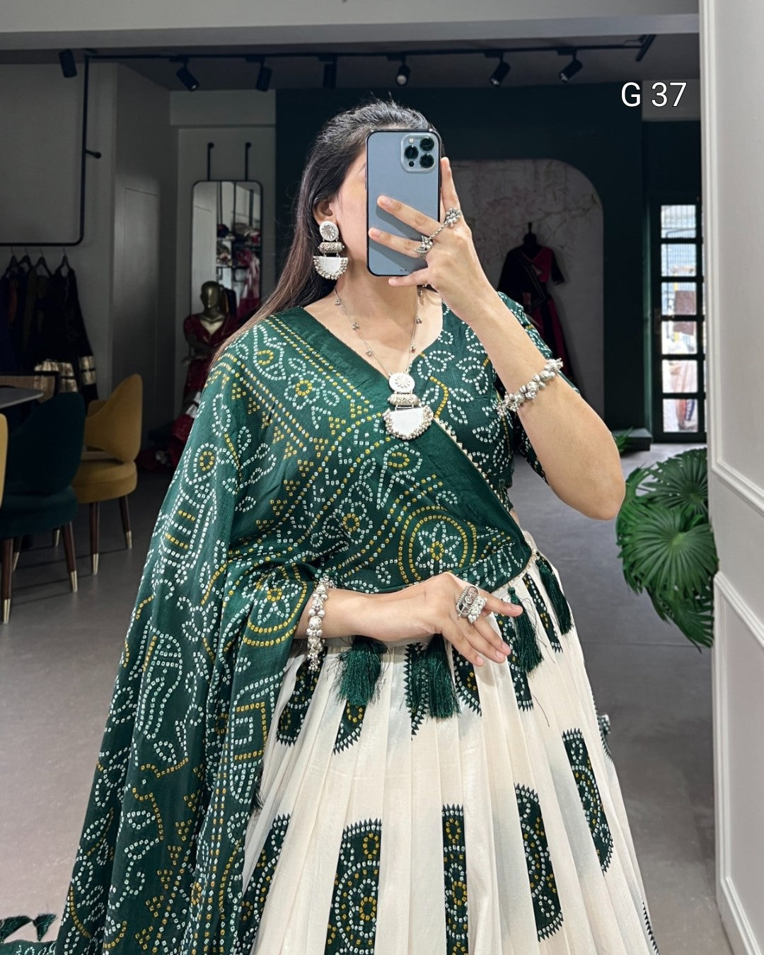 Woman wearing a green and white traditional outfit with intricate patterns, standing indoors.