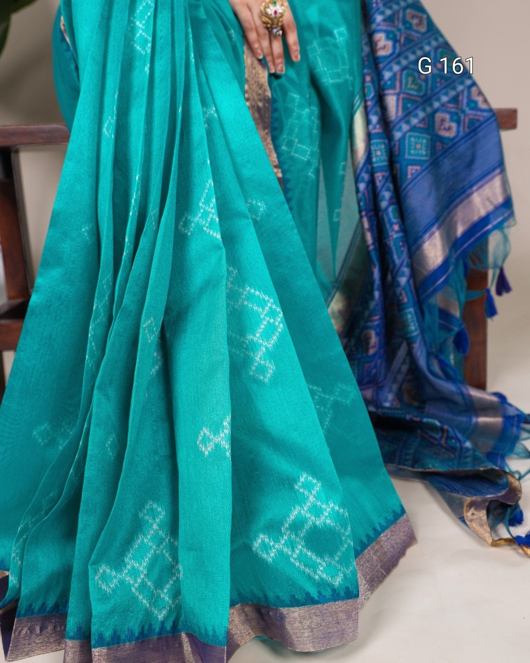 Teal saree with white patterns and blue border on a chair