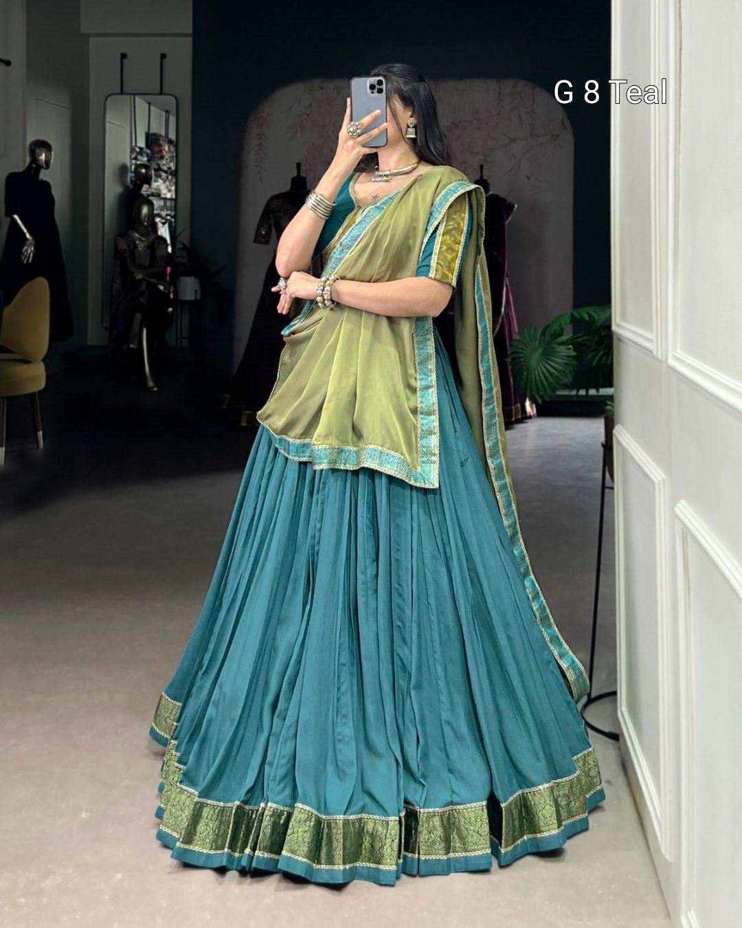 Woman wearing a teal and green traditional outfit taking a mirror selfie.