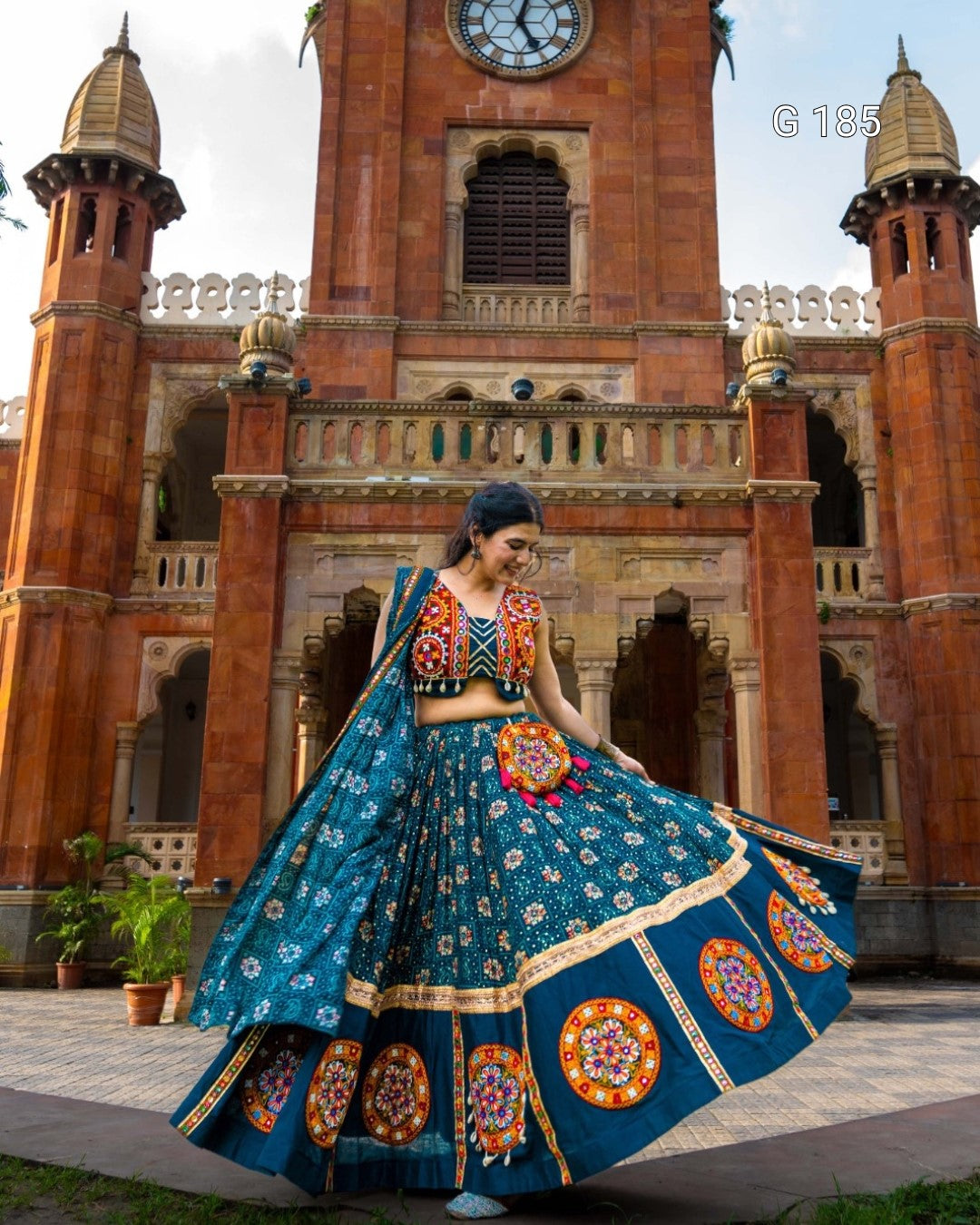 Woman in a traditional blue outfit with colorful patterns in front of a historic building.