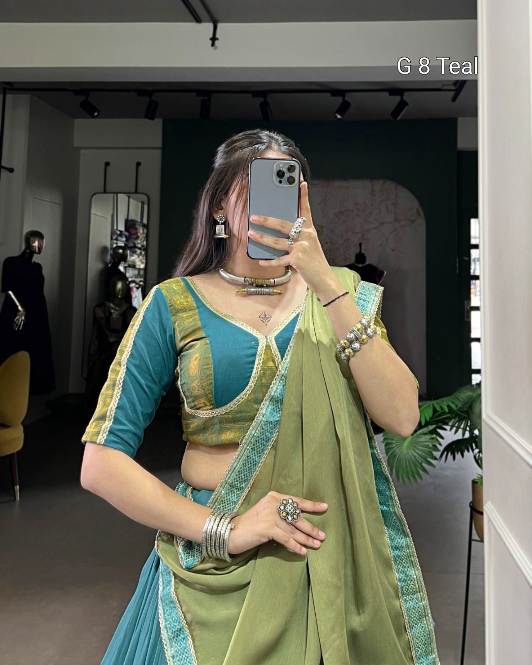 Woman taking a mirror selfie wearing a green and blue traditional outfit.