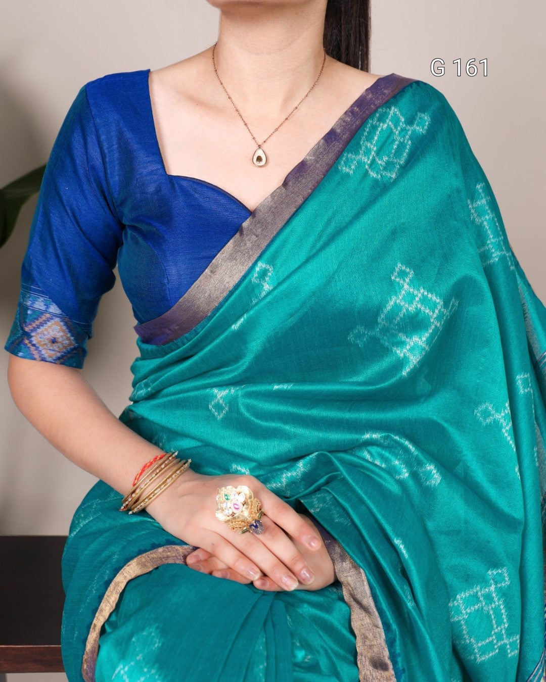 Person wearing a blue and green saree with intricate patterns, holding a ring.