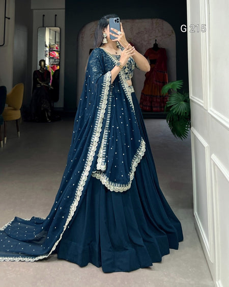 Woman in a blue embroidered saree taking a mirror selfie in a room.