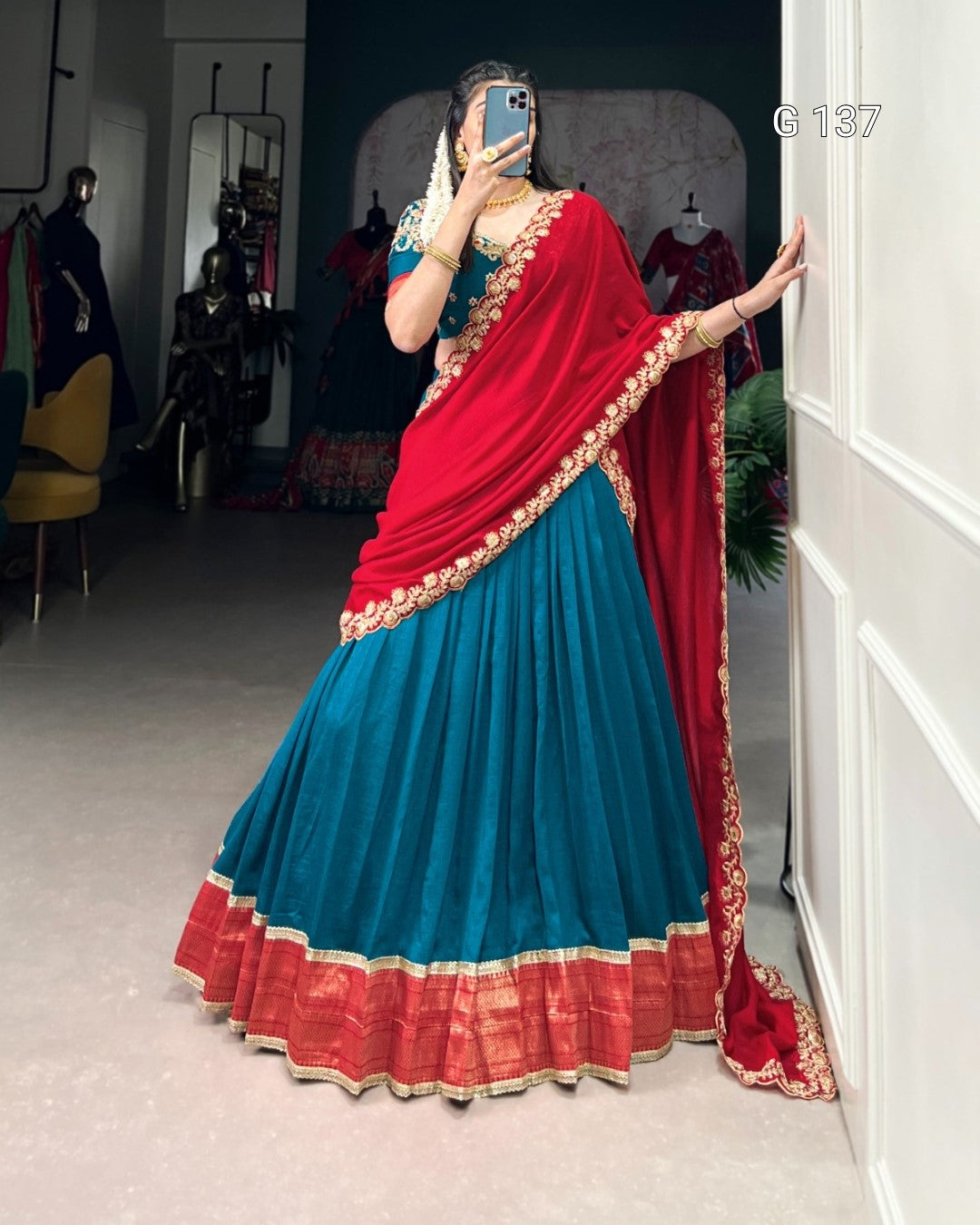 Person wearing a blue and red saree with gold border, standing in a room.