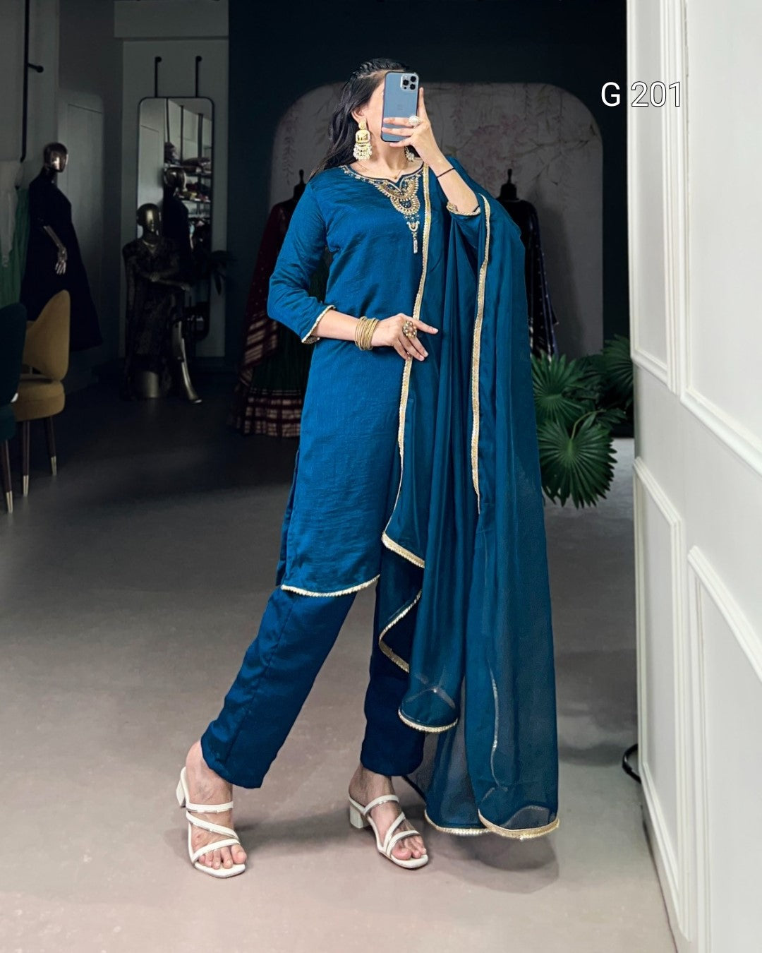 Woman in a blue traditional outfit with a scarf, standing indoors.