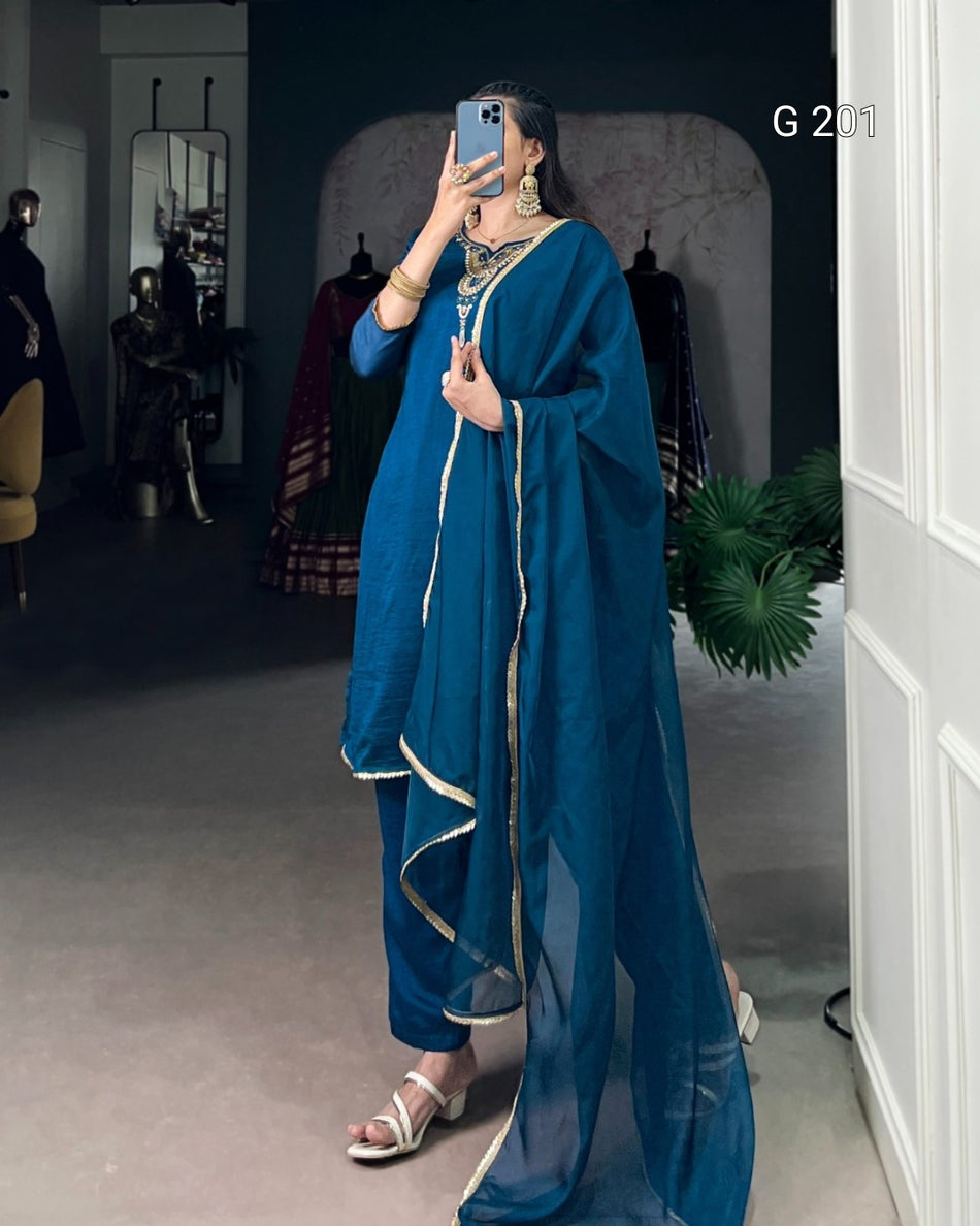 Person wearing a blue traditional outfit with gold accents in a room setting.