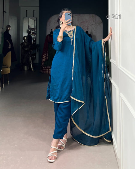 Person wearing a blue traditional outfit with gold trim in a room.