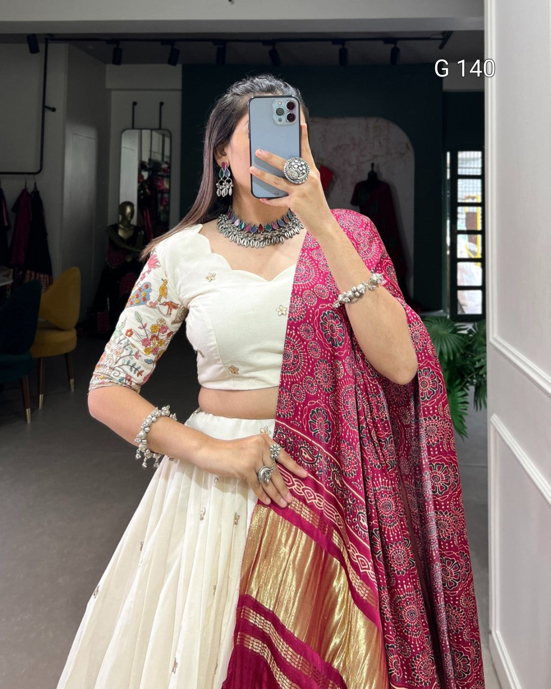Person wearing a traditional outfit with a white blouse and a red and gold saree, holding a phone.