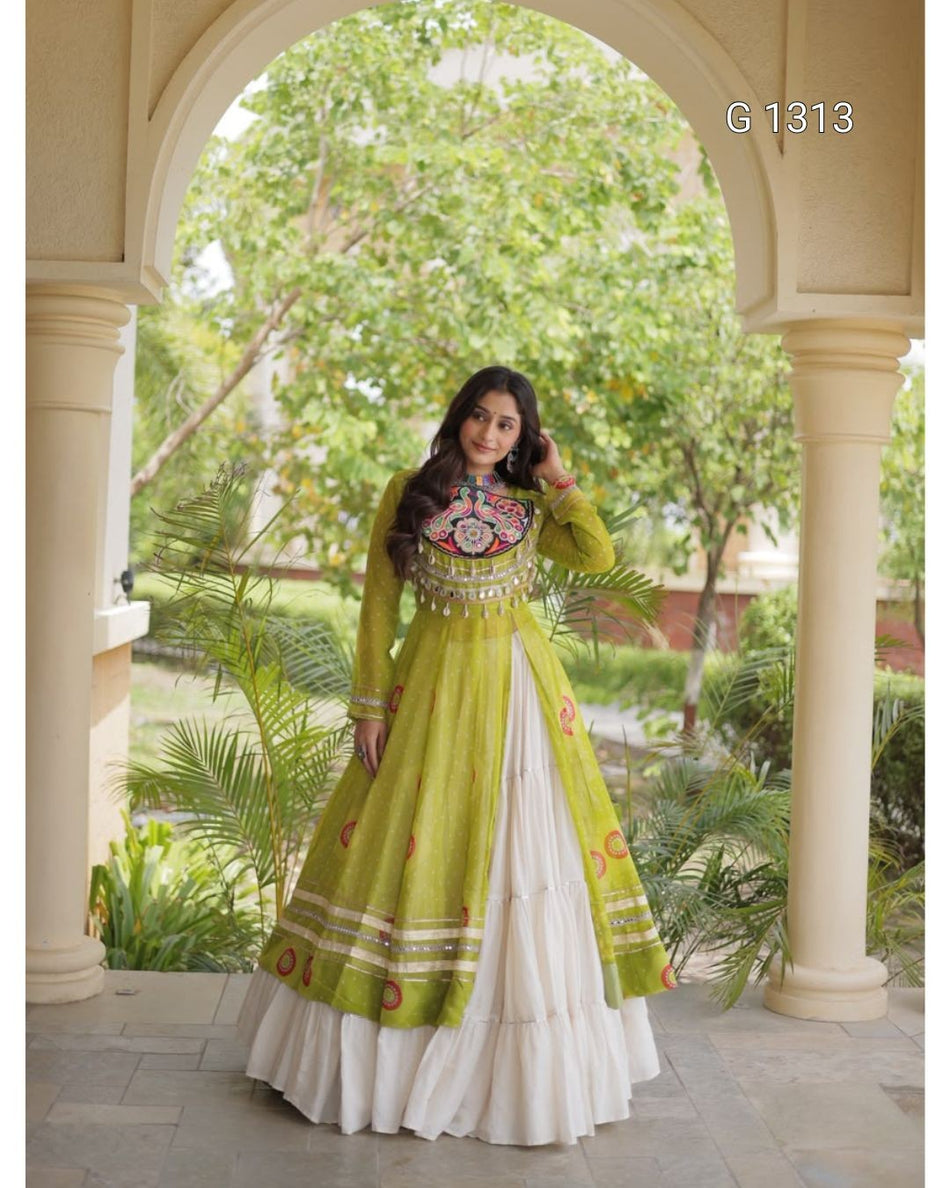 A woman models a traditional Indian anarkali gown in an outdoor arched corridor. The dress is lime green with a heavily embroidered floral bodice and a layered white flared skirt.