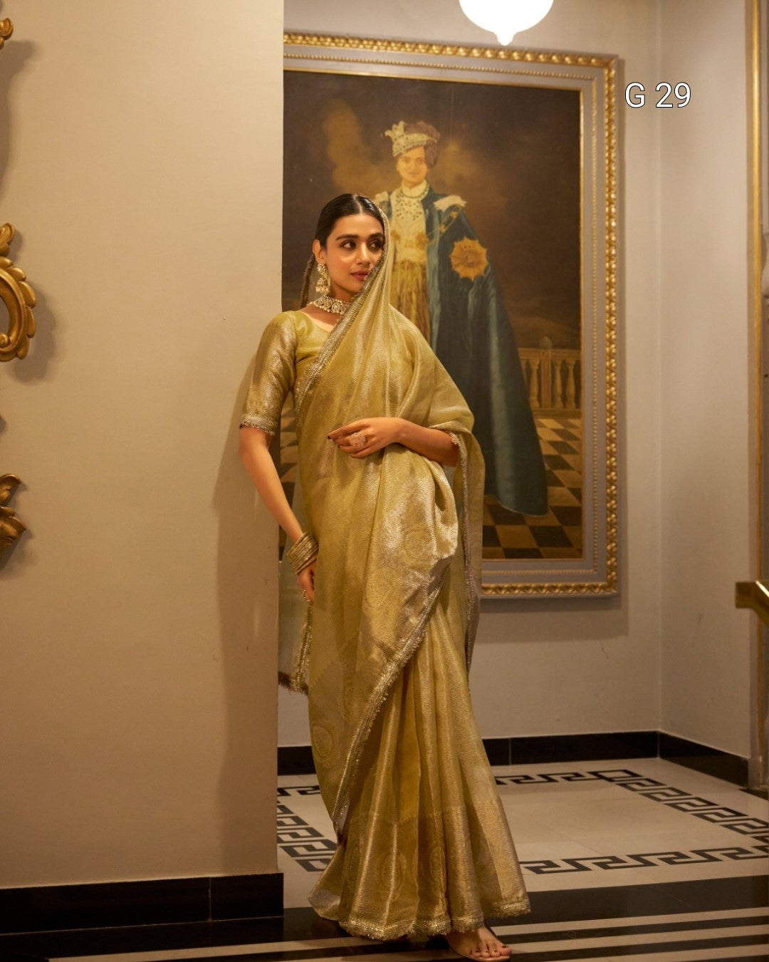 Woman in a traditional saree standing in a room with a large painting on the wall.