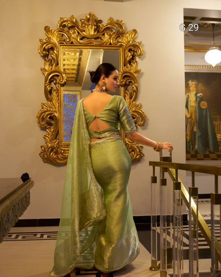 Woman in a green saree standing in front of an ornate gold mirror.