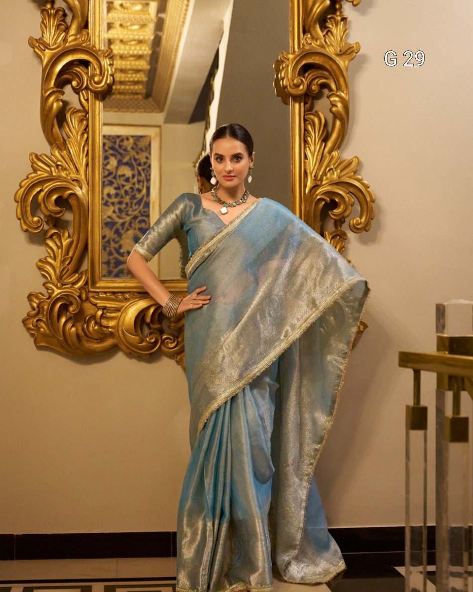 Woman in a light blue saree standing in front of an ornate gold mirror.