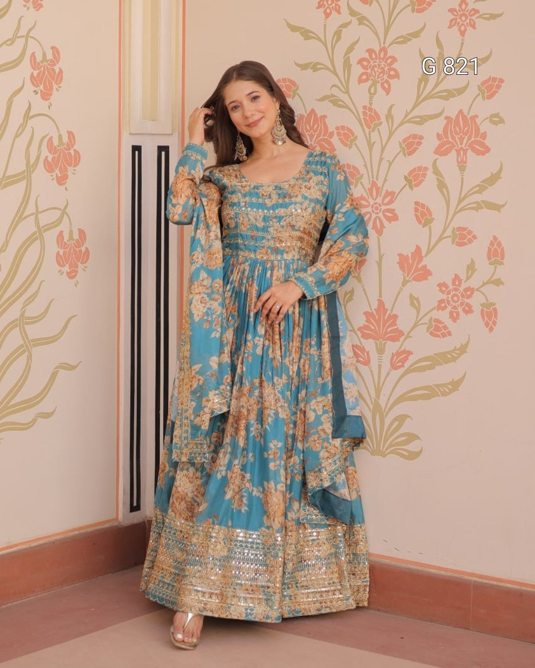 Woman in a floral dress standing against a decorated wall with floral patterns.