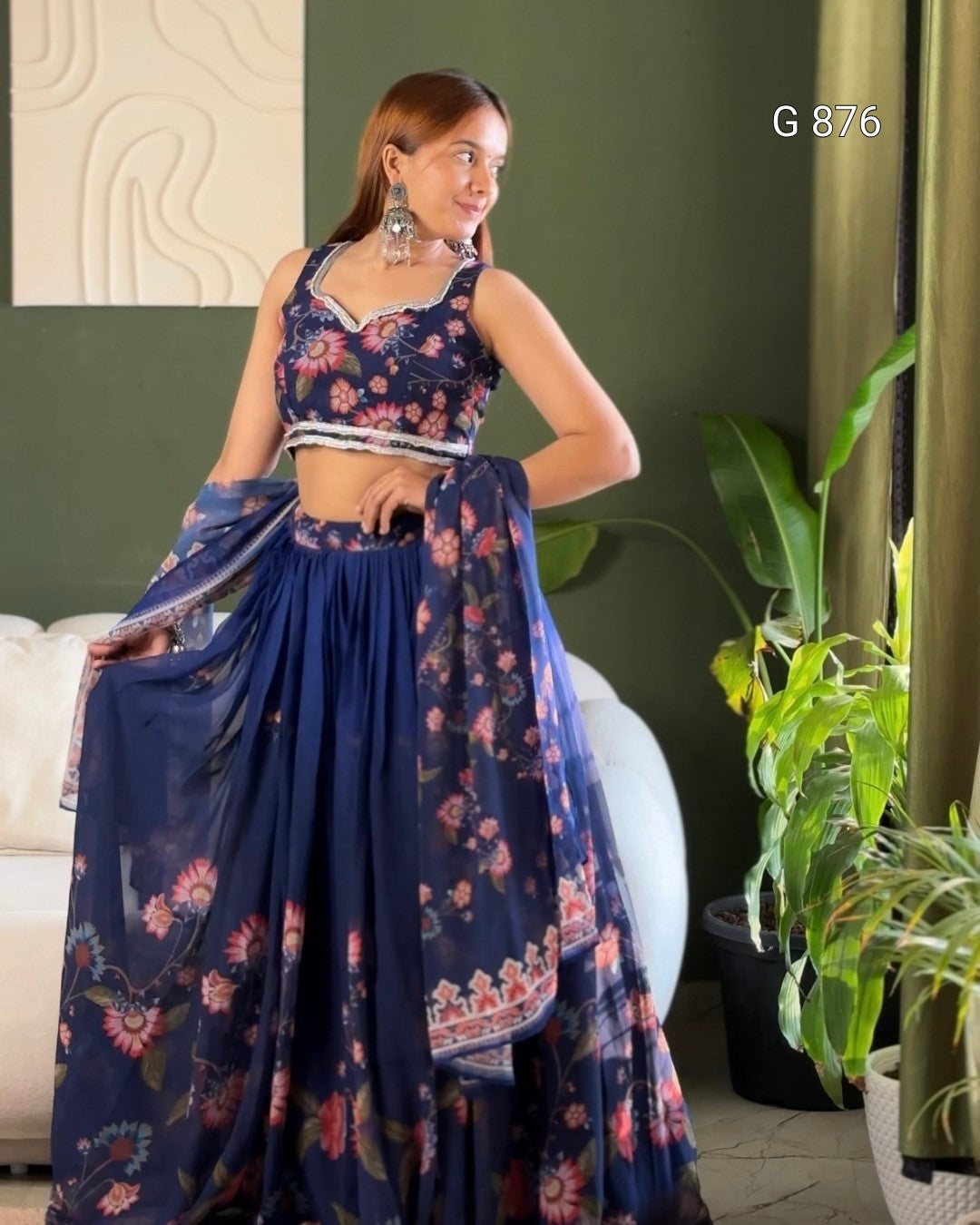 Woman in a floral saree standing in a room with green walls and plants.