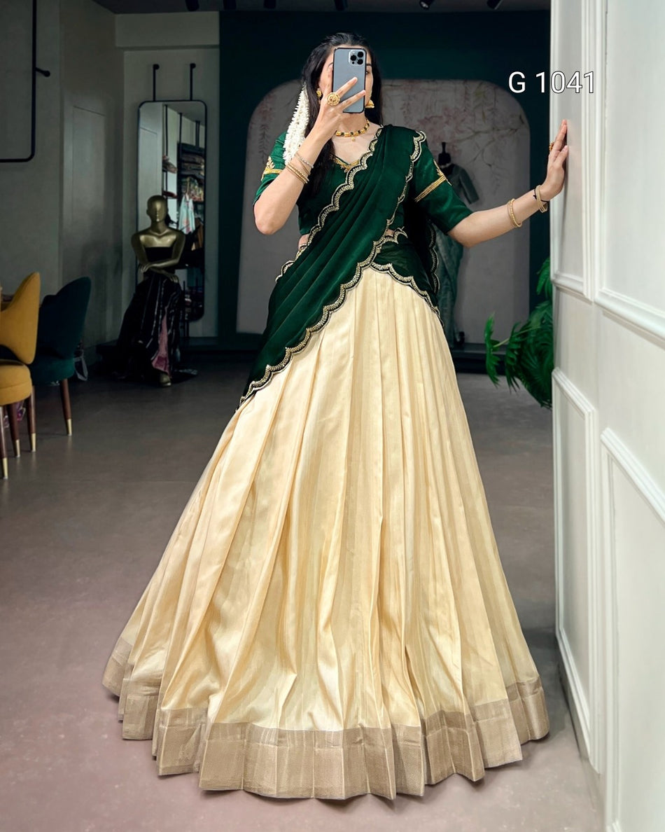 A woman takes a mirror selfie wearing a traditional Indian lehenga choli dress. The outfit features a voluminous cream-colored skirt (lehenga) with a metallic border, paired with a dark green sleeveless top (choli) and a matching draped scarf (saree drape) with gold embroidery.