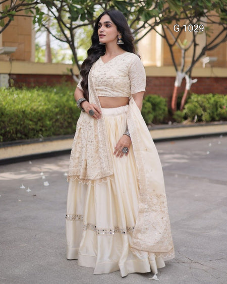 A woman modeling a cream-colored traditional Indian ethnic wear set consisting of a printed lace kurta, matching flared skirt, and draped dupatta, photographed outdoors on a paved walkway.