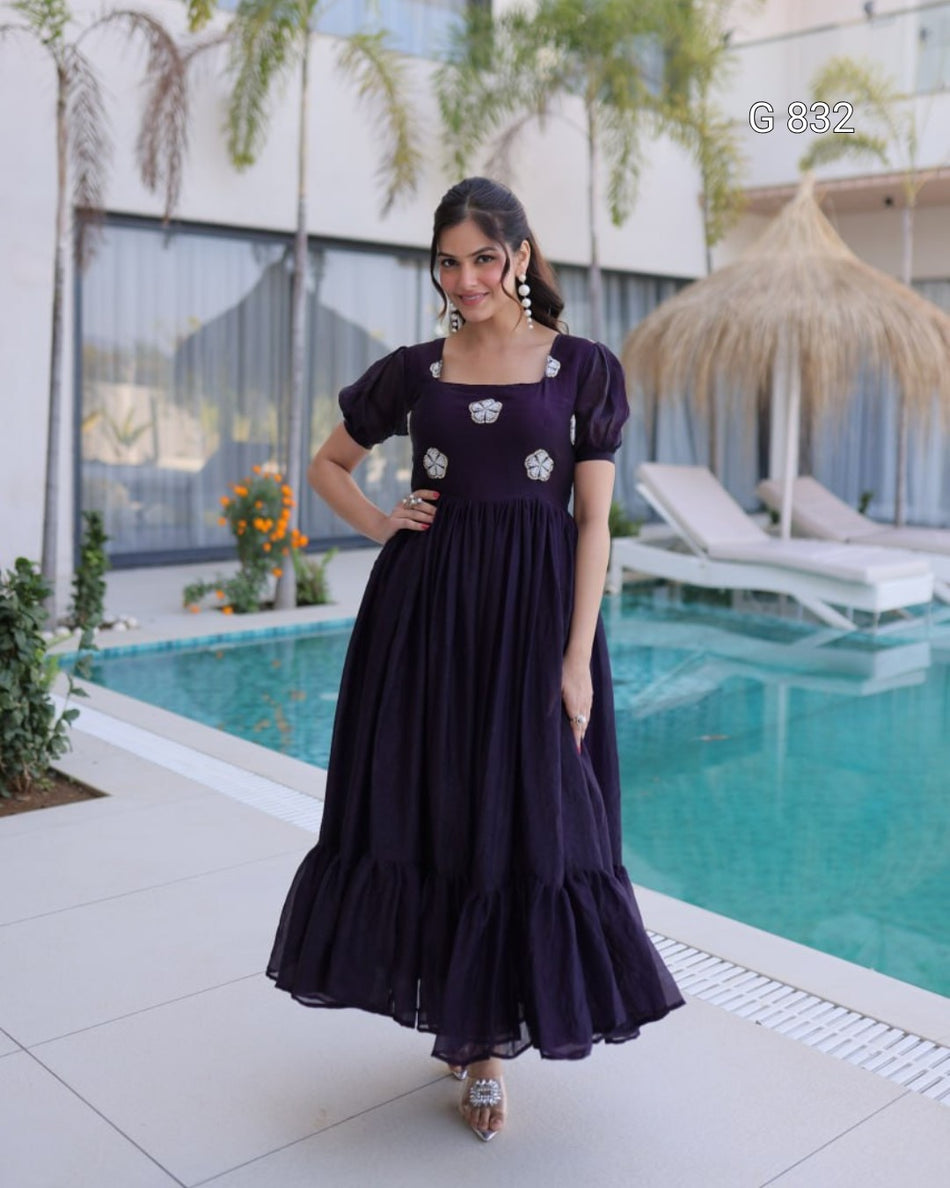 Woman in a dark purple dress standing by a poolside.