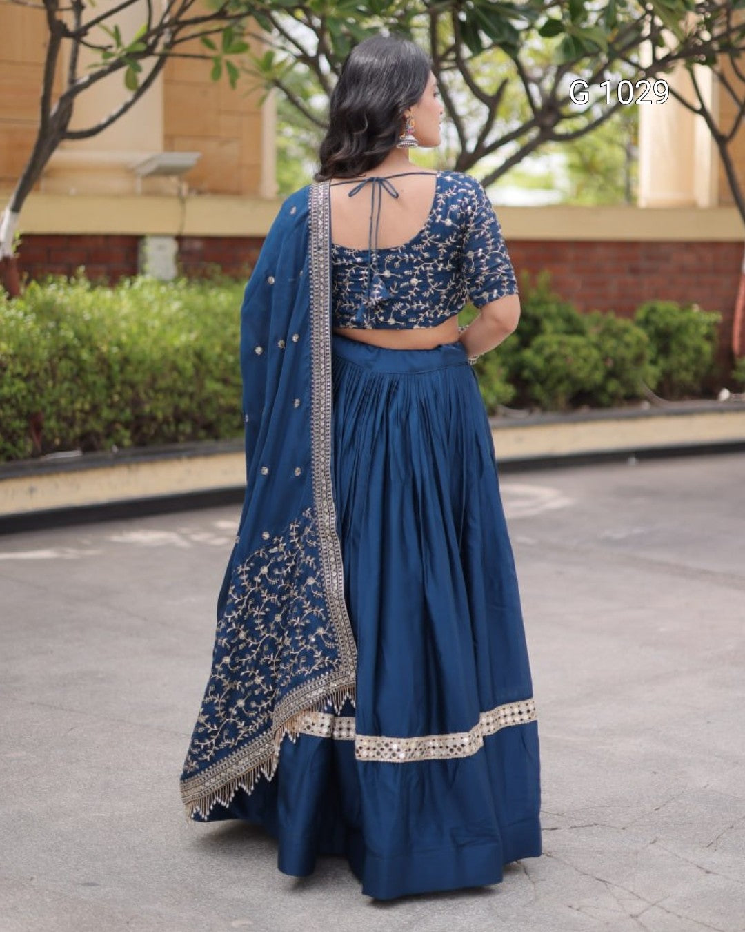A woman wearing a navy blue traditional Indian outfit with a matching skirt, blouse, and dupatta, photographed from behind in an outdoor setting.