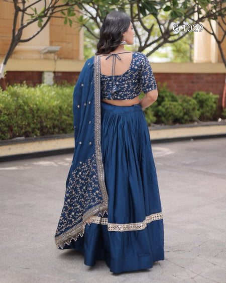 A woman wearing a navy blue traditional Indian outfit with a matching skirt, blouse, and dupatta, photographed from behind in an outdoor setting.