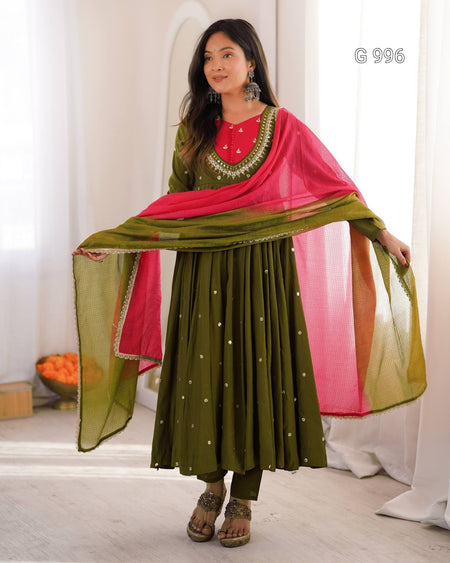 A woman modeling a traditional Indian outfit consisting of an olive green anarkali skirt with small gold embroidered dots, a red embroidered neckline, and a bright pink dupatta draped over her shoulders.
