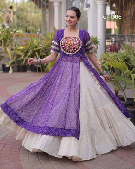 A woman modeling a traditional Indian outfit featuring a purple embroidered Anarkali-style dress with a tiered cream skirt, standing in an outdoor courtyard with potted plants.