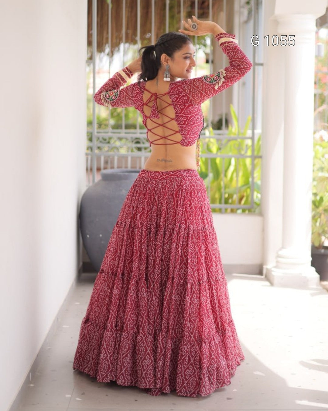 A woman modeling a traditional Indian lehenga choli dress with a dusty rose and white floral print, shown from the back in a porch setting.