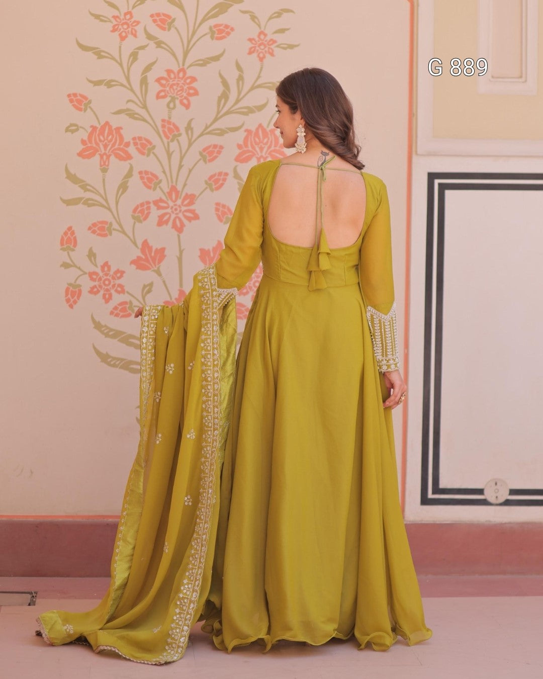 Woman in a green dress with a floral wall and pink floor in the background