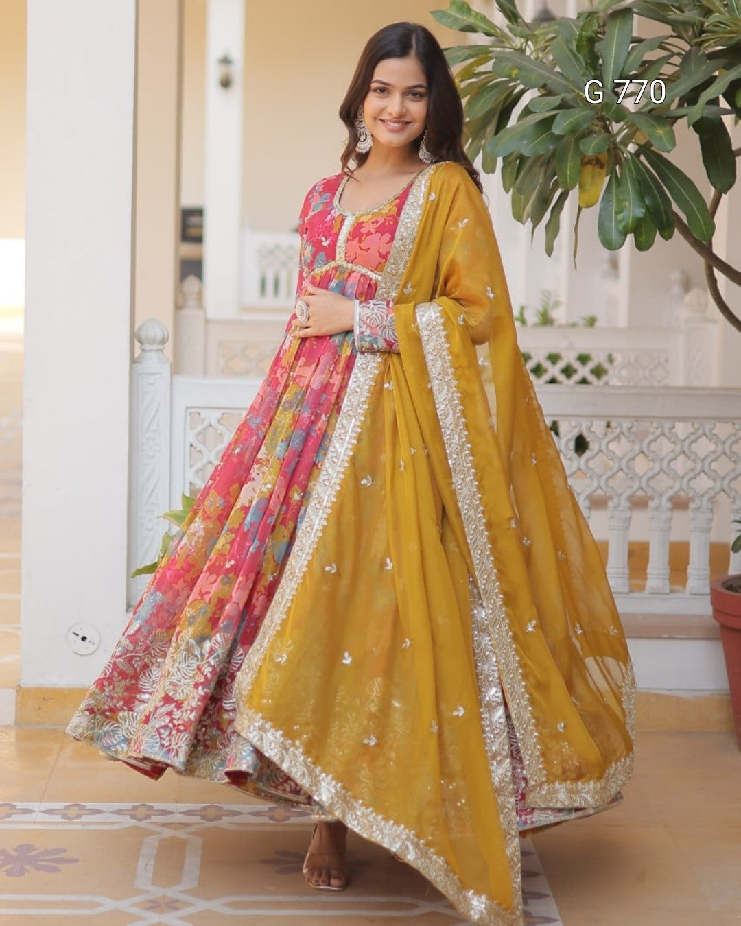 Woman in a yellow and pink traditional outfit standing on a porch.