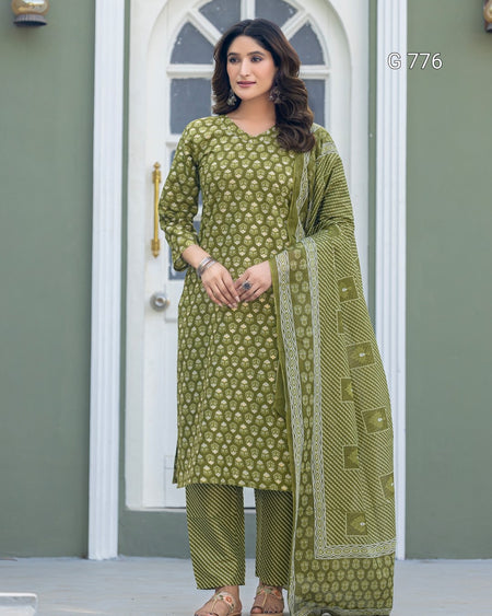 Woman wearing a green traditional outfit with a matching dupatta in front of a white door.