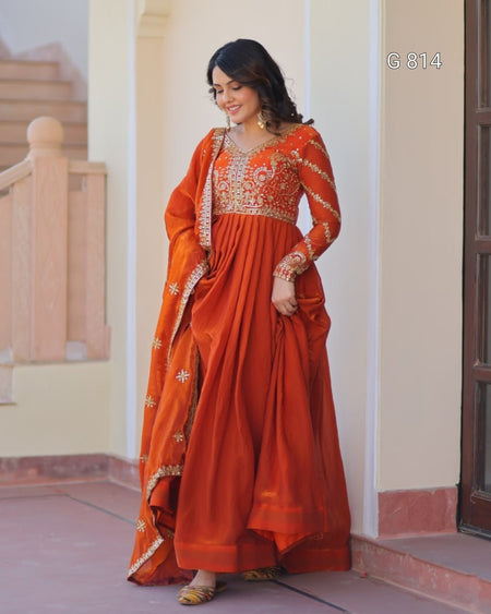 Woman wearing an orange saree with gold embroidery indoors.