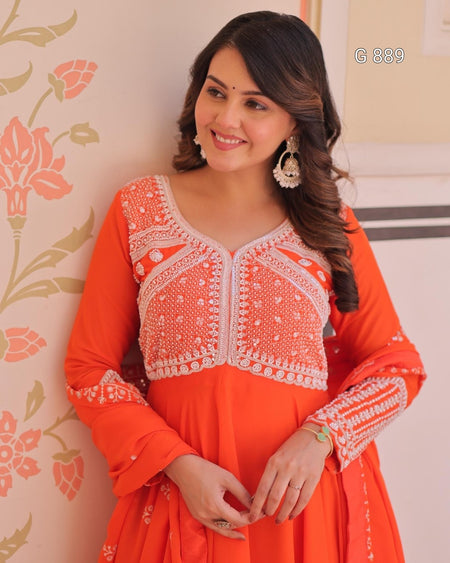 Woman wearing an orange and white embroidered traditional outfit against a floral wall.