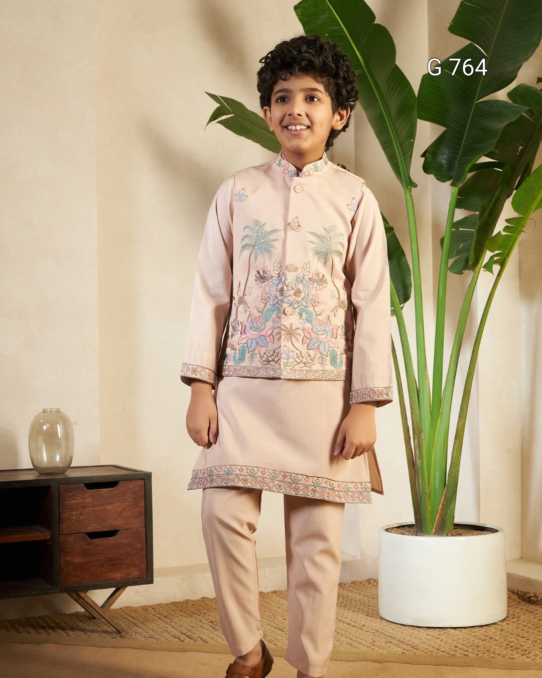 Child wearing a traditional outfit standing indoors with a plant and wooden cabinet in the background