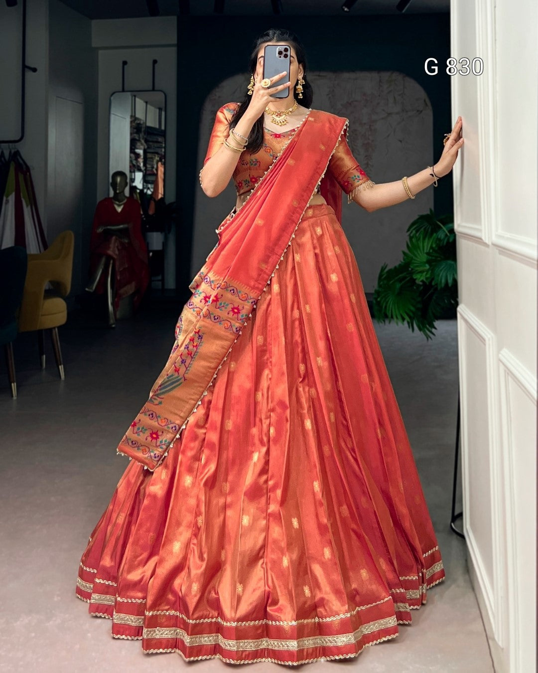 Woman in an orange saree with gold details standing in a room.
