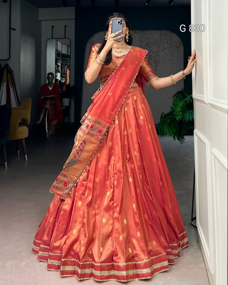 Woman in an orange saree with gold details standing in a room.