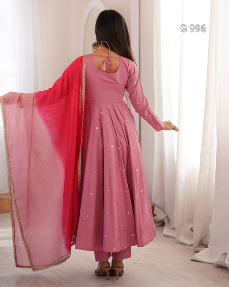 A woman wearing a pink long-sleeve anarkali dress with silver embroidered dots and a bright pink dupatta, shown from the back in a brightly lit room with white curtains.