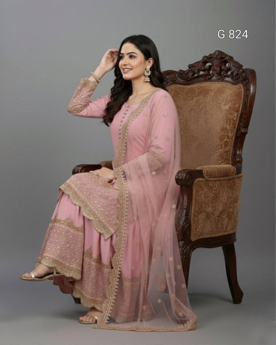 Woman in a pink traditional outfit sitting on a decorative chair against a gray background