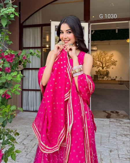 A woman wearing a bright pink traditional outfit with gold embroidery and a matching dupatta, standing in front of a building entrance. The text 'G 1030' is visible in the top right corner.
