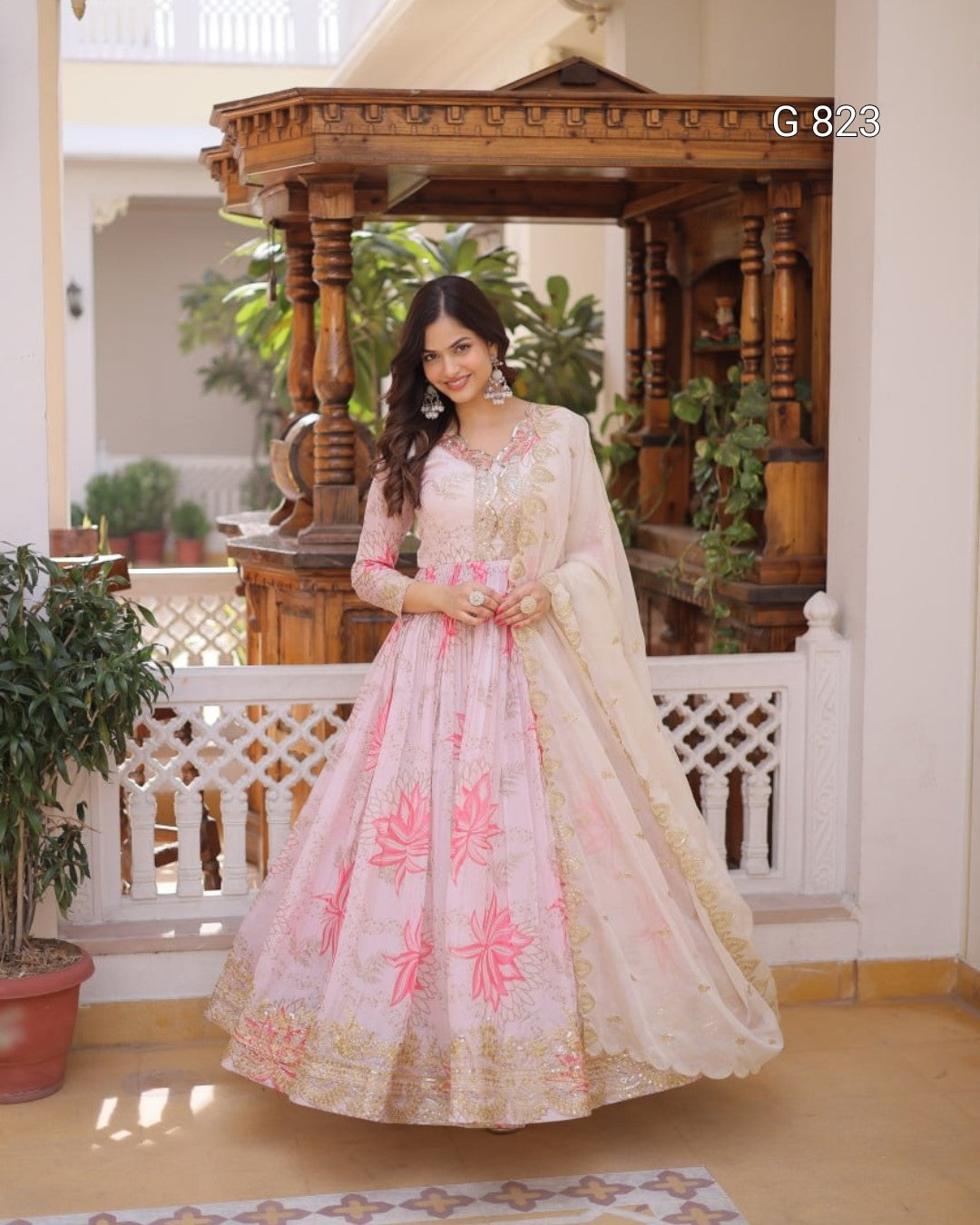 Woman in a traditional outfit standing in an indoor setting with wooden architecture and plants.