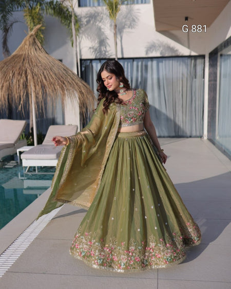 Woman in a green traditional outfit by a poolside with a building and palm trees in the background.