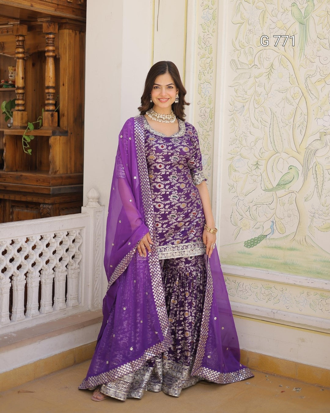 Woman in a purple traditional outfit standing in a decorated room.