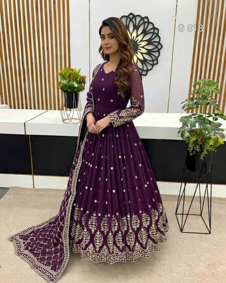Woman in a purple traditional outfit with intricate designs in a modern interior setting.